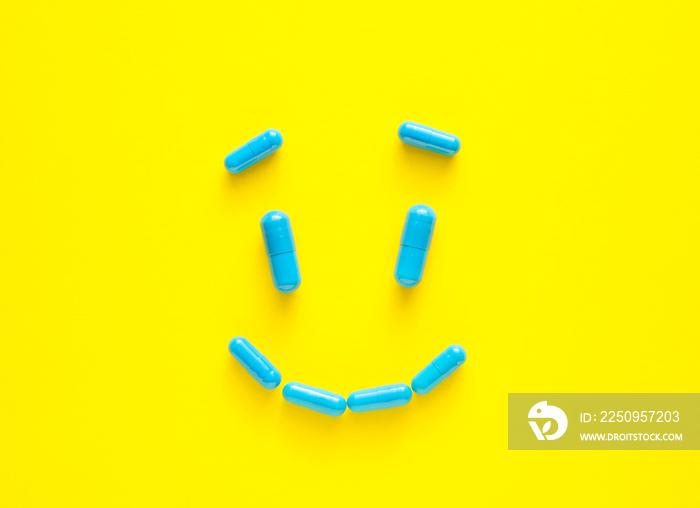 Smile made of blue pills on color background