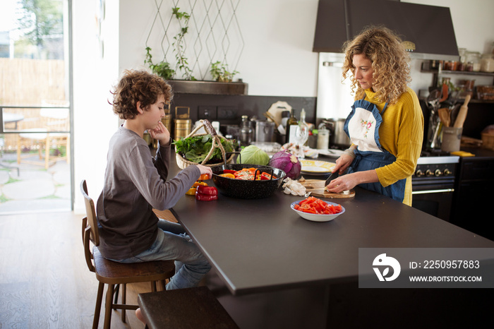 Mother chopping vegetables while son sitting by kitchen counter at home