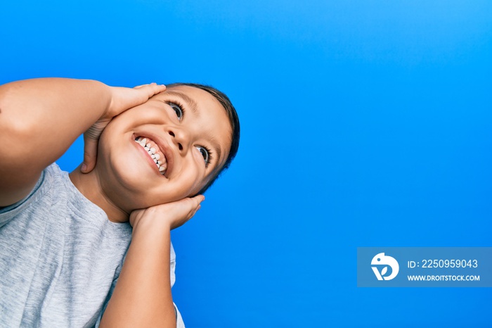 Adorable latin toddler smiling happy standing over isolated blue background.