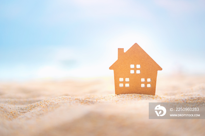 Small home model on sunset beach sand texture background.