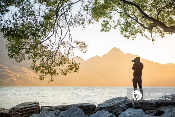 年轻的男性摄影师在皇后镇日落的黄金时段观看瓦卡蒂普湖的风景，