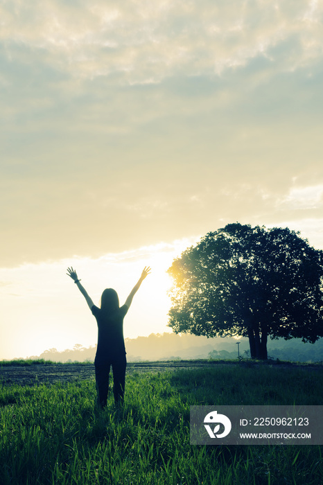 silhouette of female raise both hands up feeling happy with wacthing sun rising over grass field