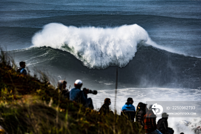 A group of people watching and photographic large stormy waves on the sea near Nazare, Portugal