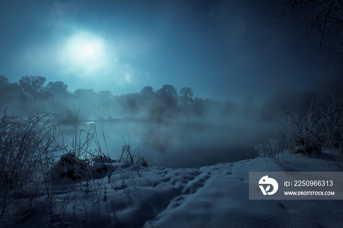 夜晚神秘的风景。雾蒙蒙的河流上的满月。白雪覆盖的河岸。