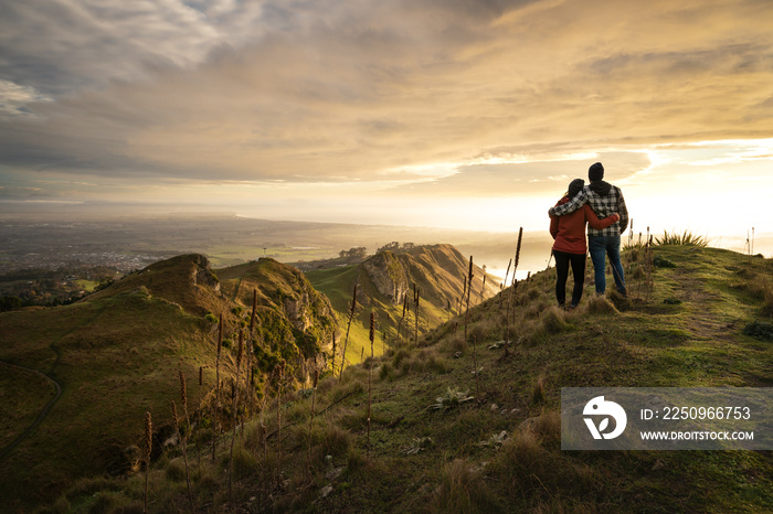 Man and woman embracing each other on the peak on a mountain while contemplating the landscape