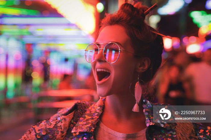 Woman wearing sparkling jacket on the city street with neon lights