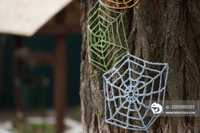 Blue and green knitted cobwebs on a tree trunk close-up.