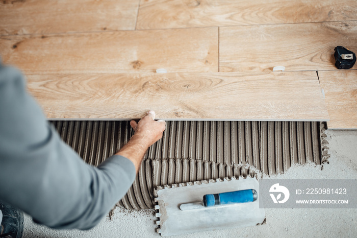 Flooring and tiling. Professional tiler placing floor tiles on adhesive surface.