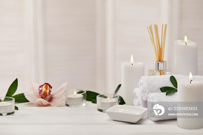 Spa with aromatic candles, orchid flower and towel on white wooden table. Beauty spa treatment and r