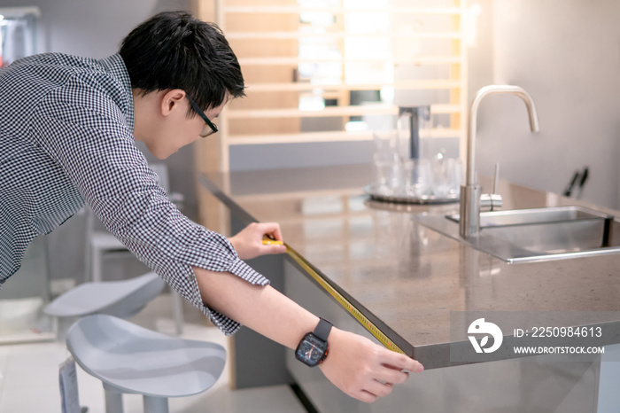Young Asian man using tape measure for measuring granite countertops on modern kitchen counter in sh