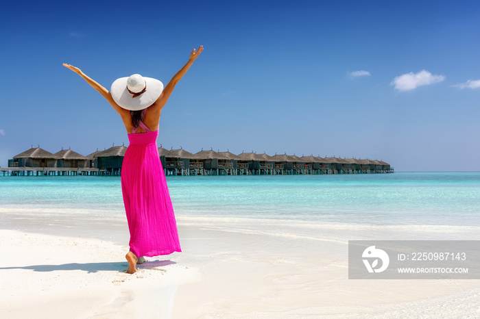 Glückliche Frau im pinken Sommerkleid genießt den Ausblick auf einen tropischen Strand mit türkisem 