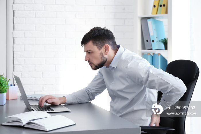 姿势概念。一名男子在办公室用笔记本电脑工作时背部疼痛