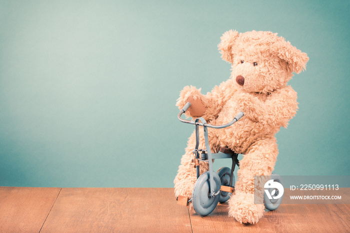 Teddy Bear is sitting on old retro toy bicycle in front mint green background. Vintage style filtere