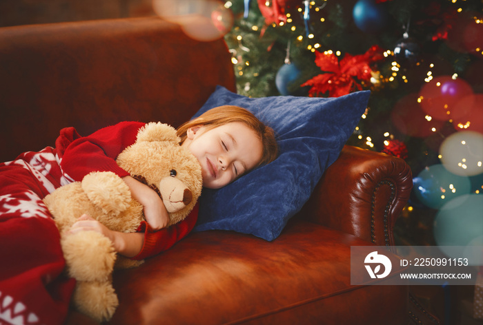 Little girl sleeping near illuminated xmas tree