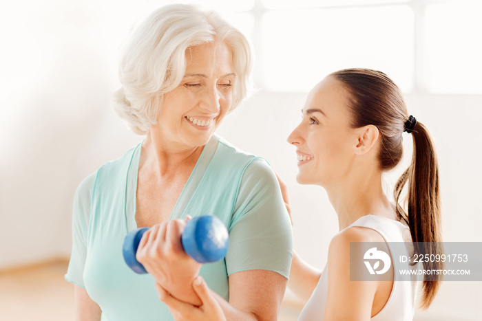 Nice fitness coach helping the elderly woman