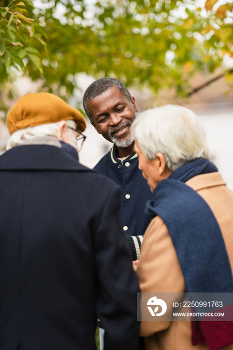 Smiling african american man looking at blurred multiethnic friends in park.