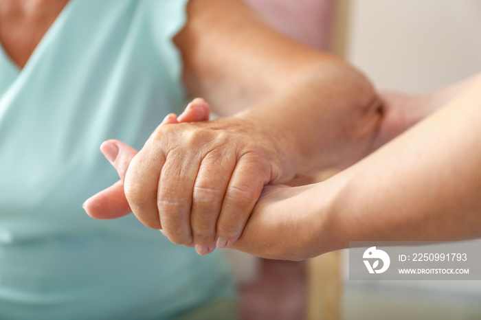 Young daughter supporting elderly mother at home, closeup