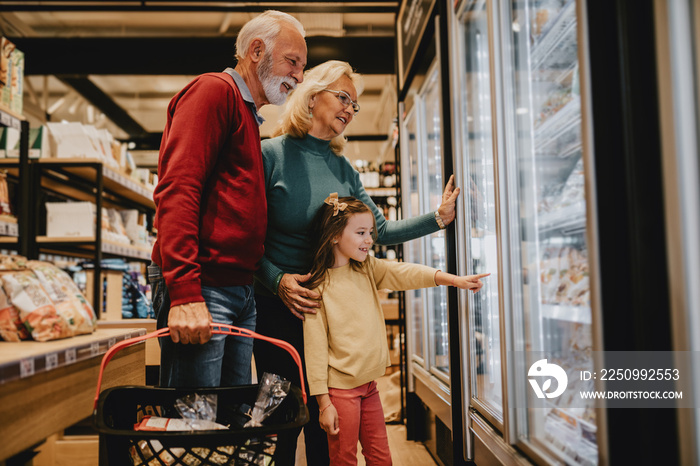 Happy grandmother and grandfather with granddaughter shopping together in grocery store or supermark