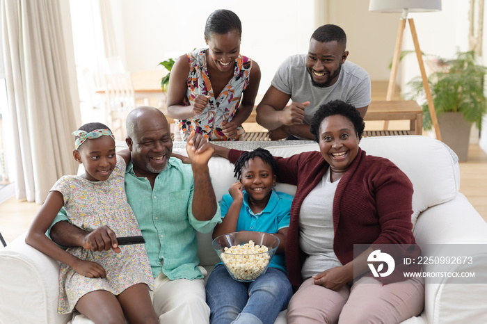 Excited african american parents, grandparents and grandchildren on couch watching tv and cheering