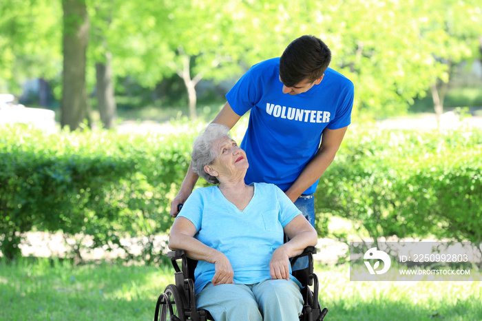 Happy senior woman on wheelchair with young male volunteer outdoors