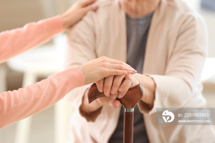 Old and young women holding hands on walking stick, closeup