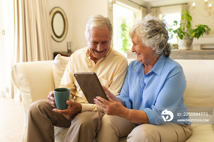 Senior caucasian couple sitting on sofa using tablet