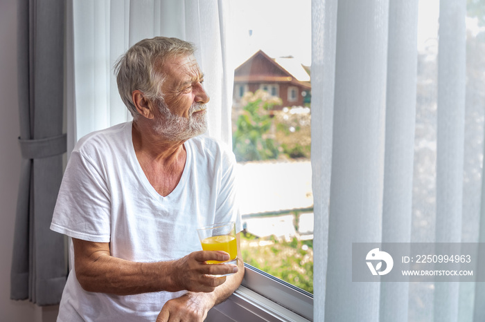 Senior elderly man standing and looking out of window in bedroom after waking up in morning with jui