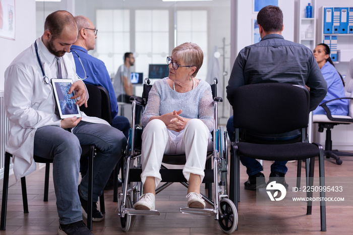 Doctor man sitting in waiting hospital area with senior disability woman discussing recovery treatme