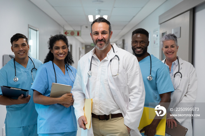 Portrait of diverse group of male and female doctors holding files, smiling in hospital corridor