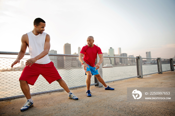 Two men exercising by riverside cityscape in background