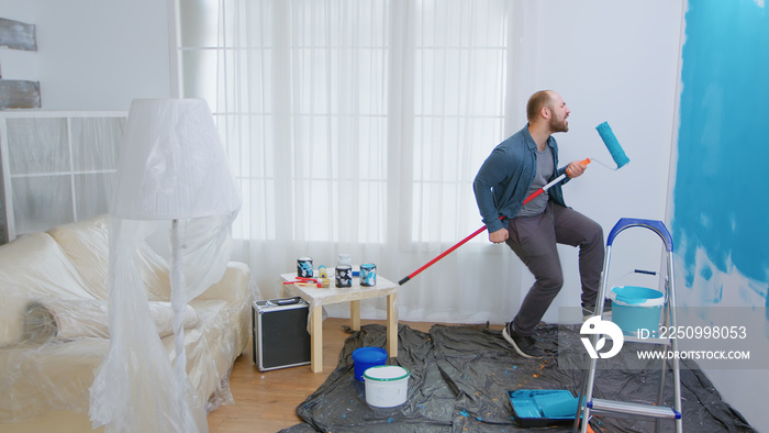 Repairman during home construction using roller brush as guitar. Guy singing while renovating house.