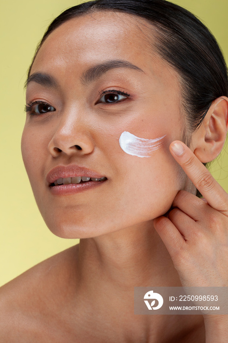 Studio shot of woman applying face cream on cheek