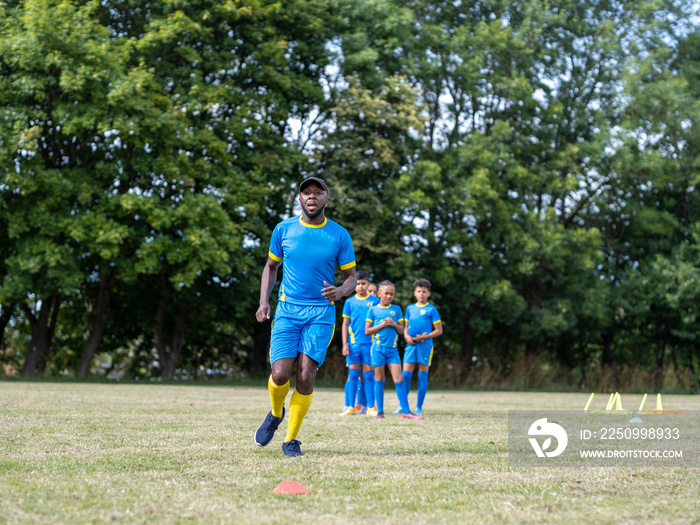 穿着制服的儿童（8-9岁）和教练在足球场上练习