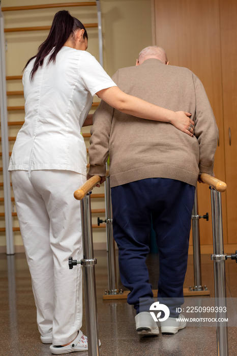 Rear view of physiotherapists assisting stroke patient with parallel equilibrium bars.