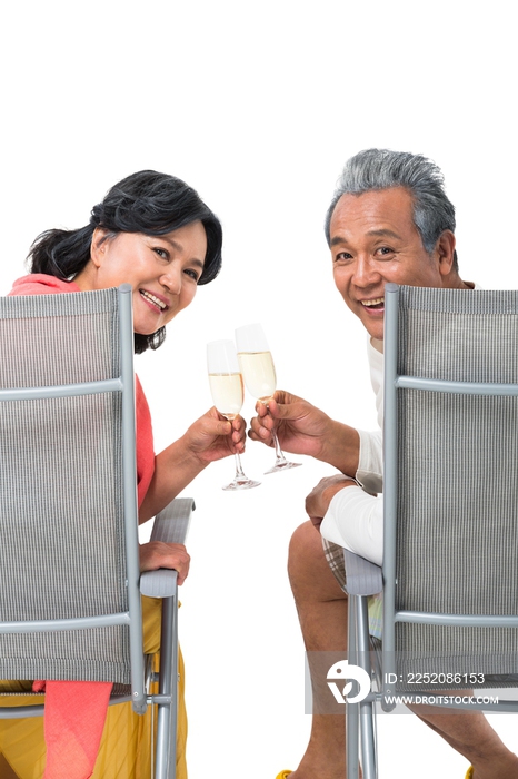 快乐的老年夫妇坐在沙滩椅上喝香槟酒