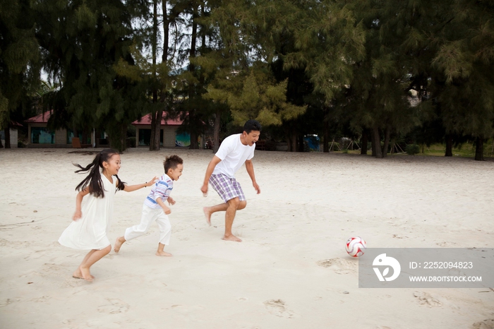 中年人和小女孩、小男孩在海边踢足球