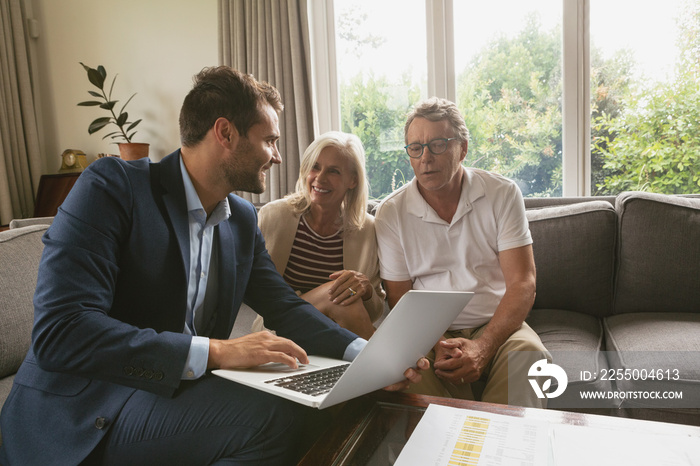 Active senior couple discussing with real estate agent over laptop in living room