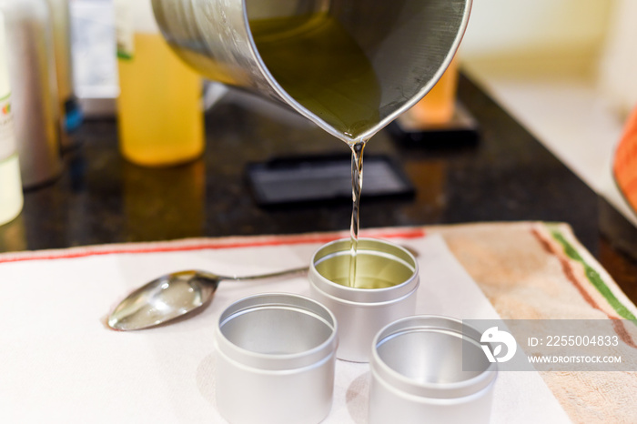 Creative occupation of candle making showing the pouring of liquid wax into jars