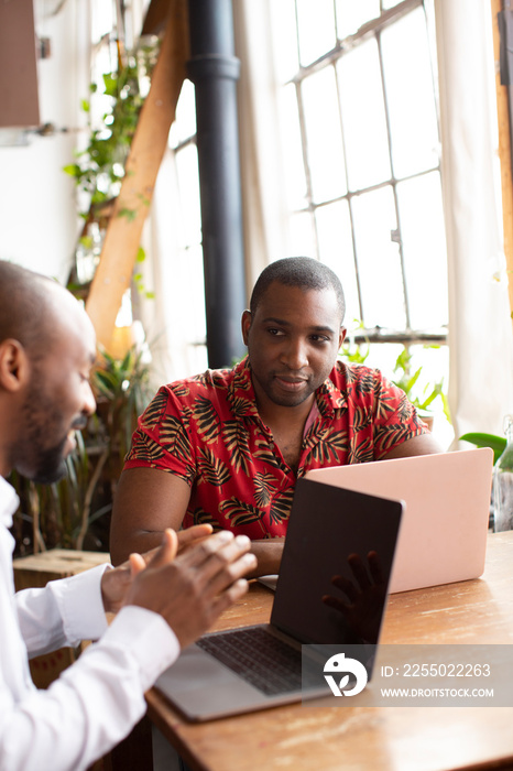 Smiling businessman explaining to male coworker over laptop computer on wooden table at home office