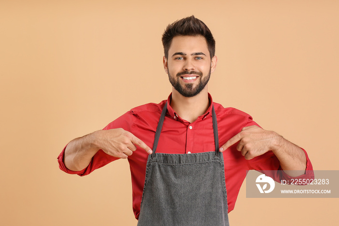 Young man in apron on color background