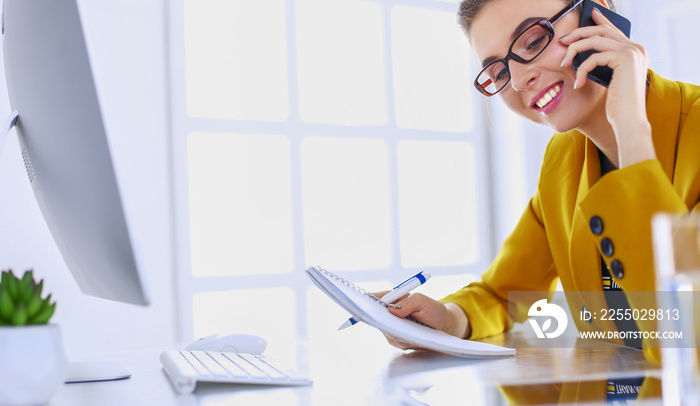 Portrait of beautiful woman making call while sitting at her workplace in front of laptop and workin