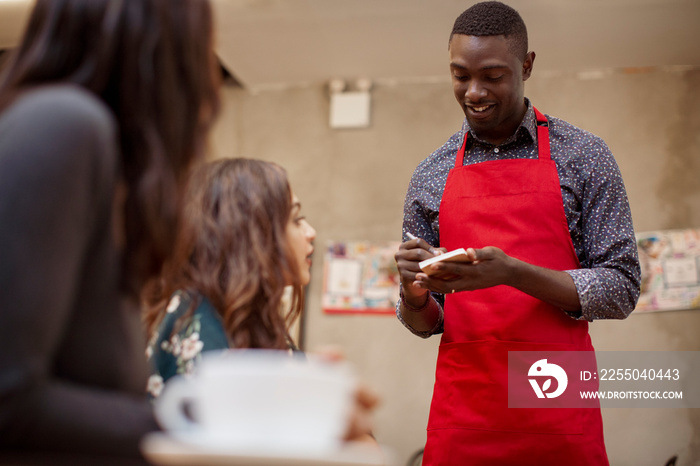 Smiling waiter taking order from female customers while standing in restaurant