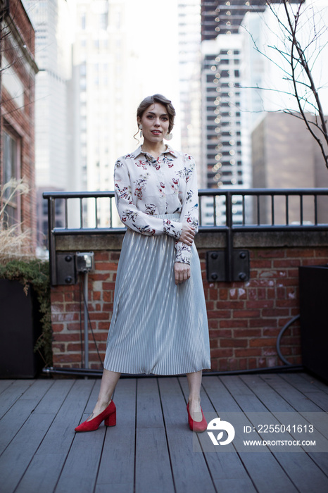 Portrait of confident fashionable businesswoman wearing skirt standing on hardwood floor against bui