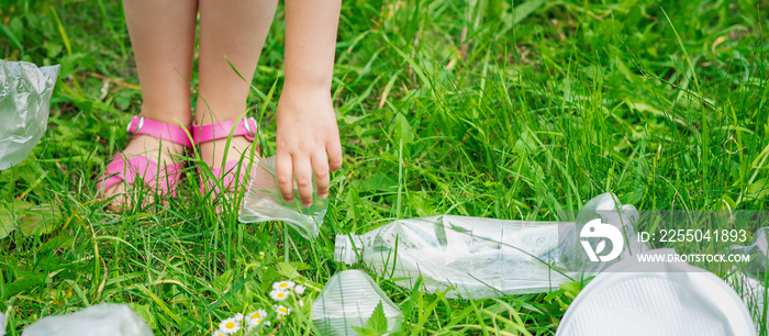 Hand of child cleans green grass from plastic trash in the park