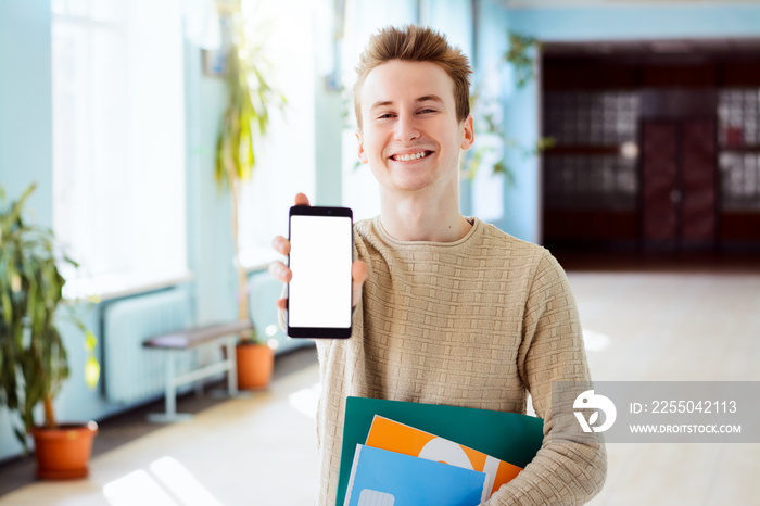 Portrait of cheerful, positive, attractive student guy having smart phone with white screen in hand,