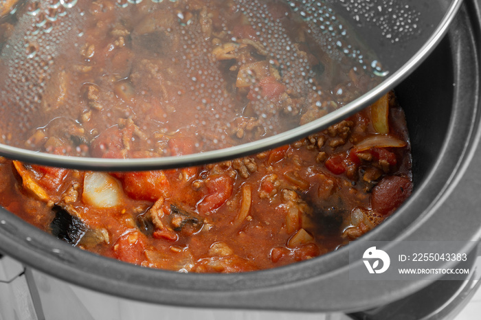 Bolognese sauce cooking in a slow cooker with glass lid lifted off.  Selective colour