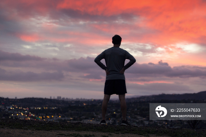 运动员在日落时观看城市景观的后视图