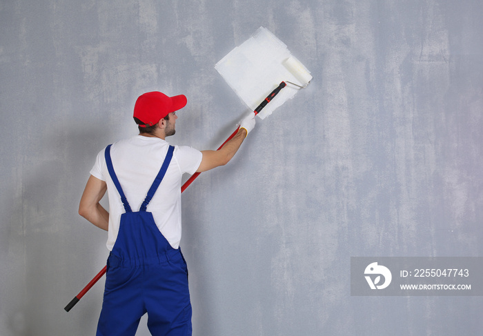 Young worker painting wall in room