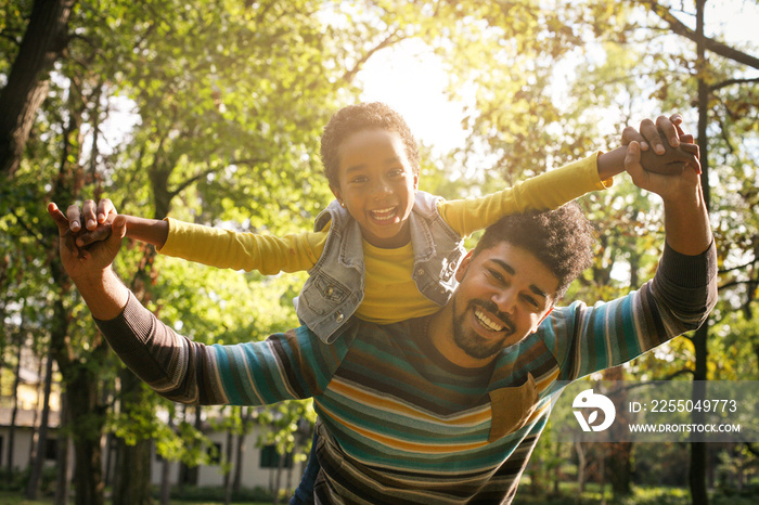 Smiling African American father carrying his daughter on piggyback and holding hands.