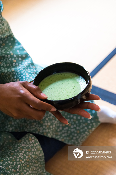 在日本传统茶道上，黑人妇女双手接过抹茶